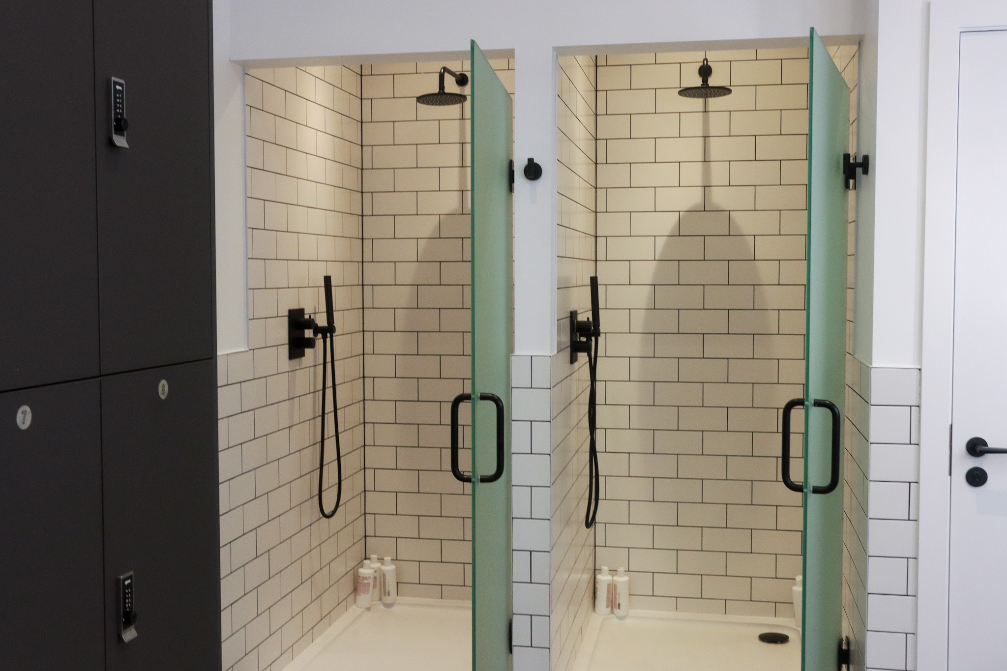 Two shower cubicles next to each other with white tiles.
